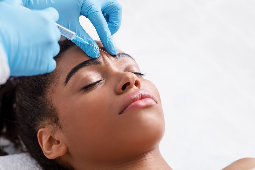 Young african woman receiving botox injection in interbrow